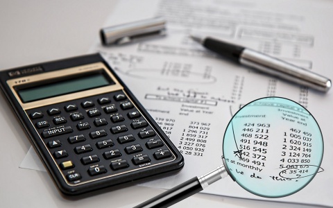 magnifying glass over part of a balance sheet, with calculator and pen